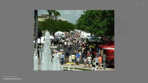 Image of pedestrian shopping and restaurant area called "The Walk" in Coral Springs. Showing a fountain, people and Art Fair in progress.