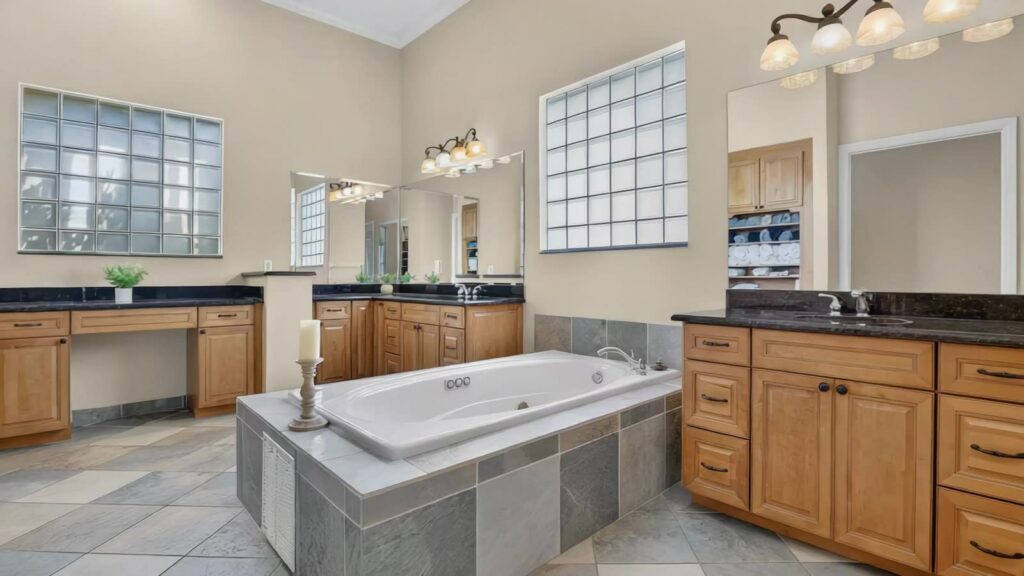 Primary bathroom with dual sinks and a whirlpool tub set under glass block