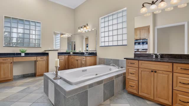Primary bathroom with dual sinks and a whirlpool tub set under glass block